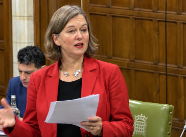 Fleur Anderson, in a red jacket, speaks from notes in Westminster Hall, with another MP seated behind her