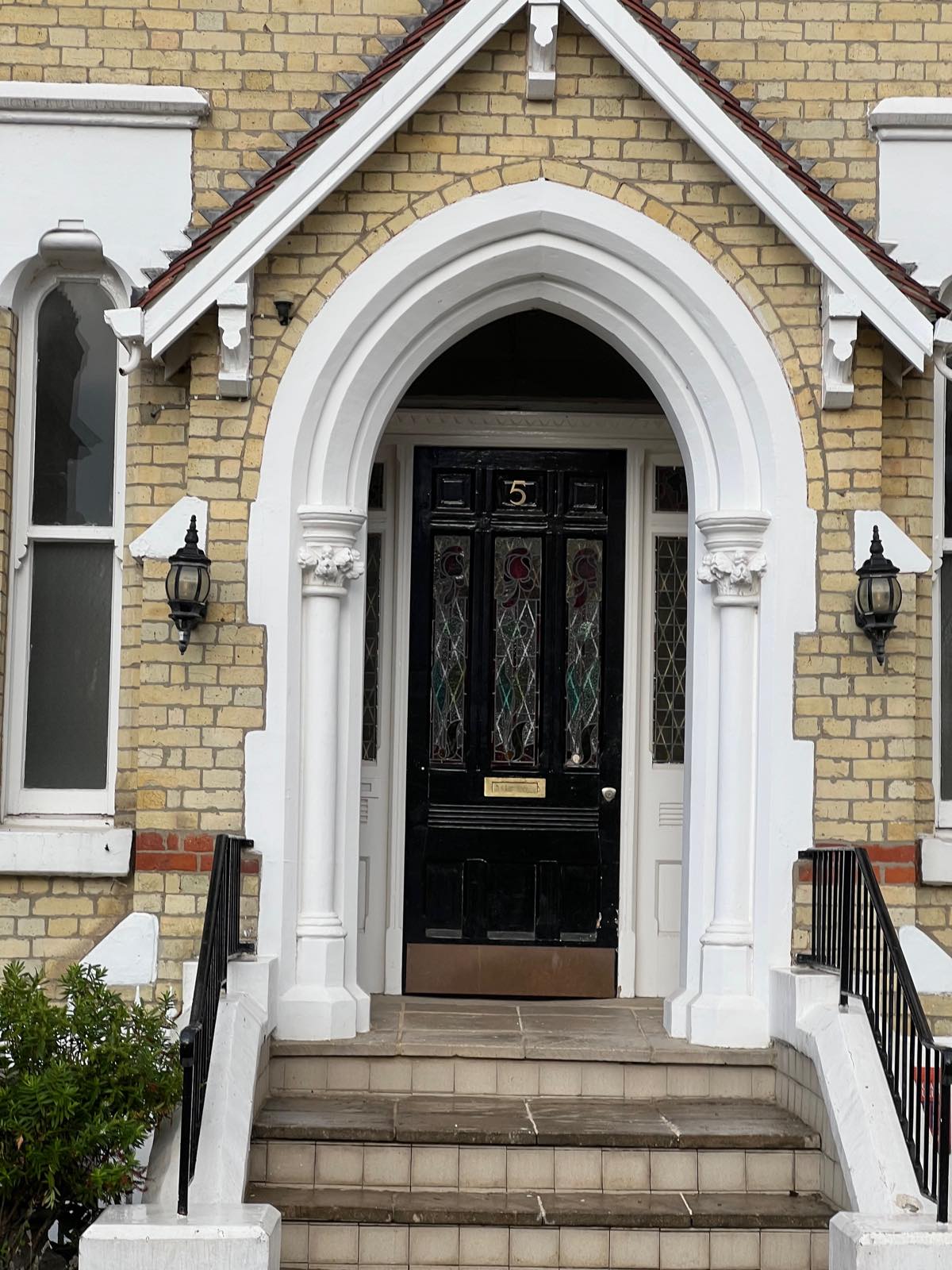 Gothic arched porch with a black stained-glass door numbered 5