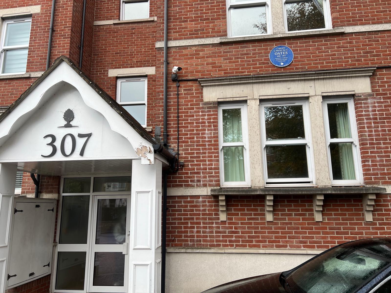 Red-brick block of flats numbered 307 with a blue plaque above a bay window