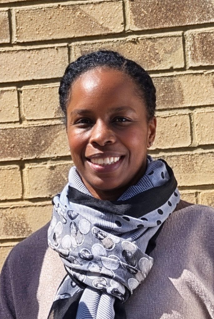 The Revd Sharon Hunt, smiling, in a patterned scarf against a brick wall