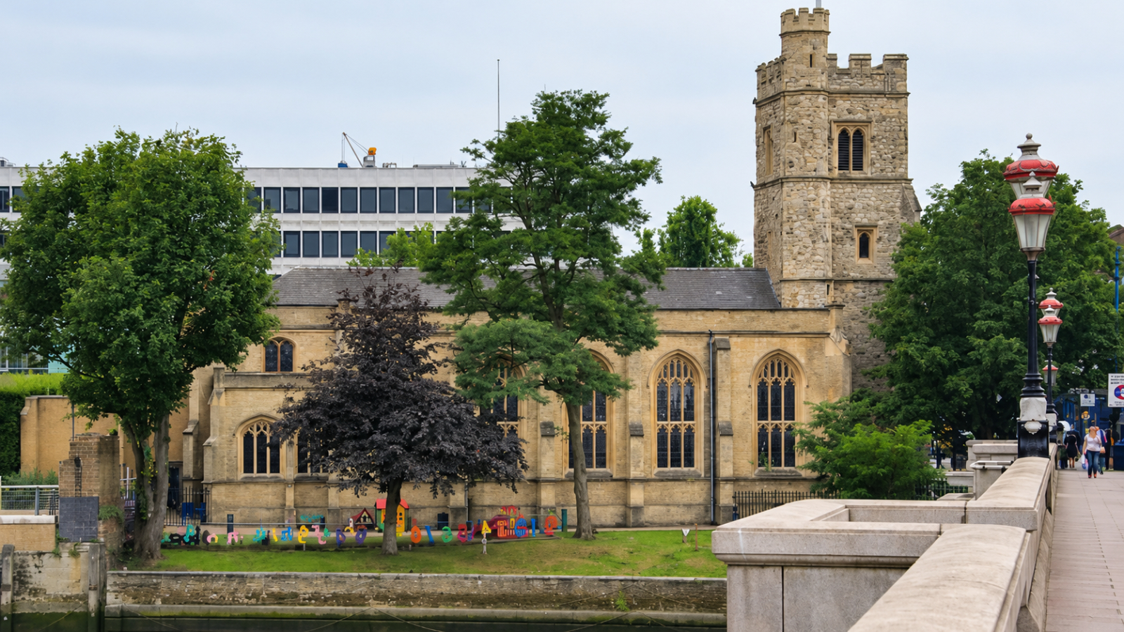 St Mary’s Church in Putney seen from Putney Bridge, with its stone tower, tall windows and trees beside the river