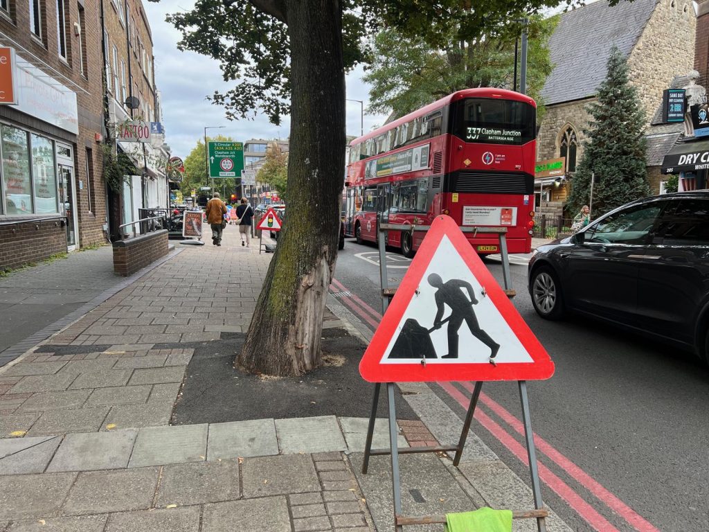 Double red lines at the kerb of Upper Richmond Road beside a roadworks sign