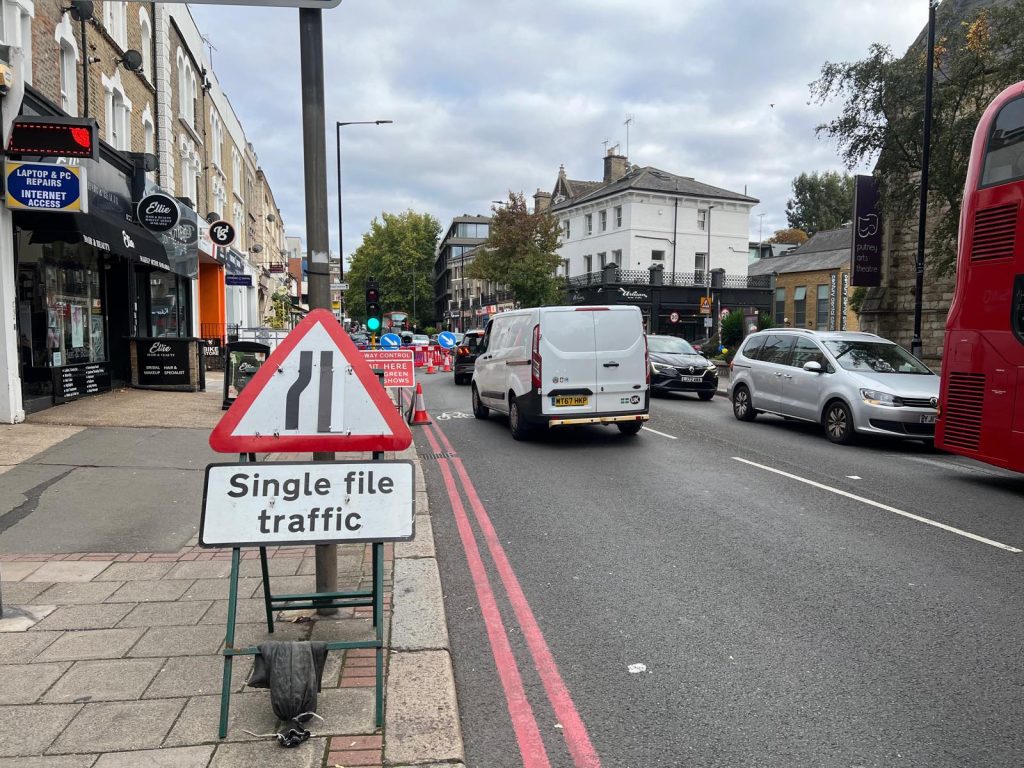 A temporary road sign reading Single file traffic on Upper Richmond Road, with red route lines at the kerb