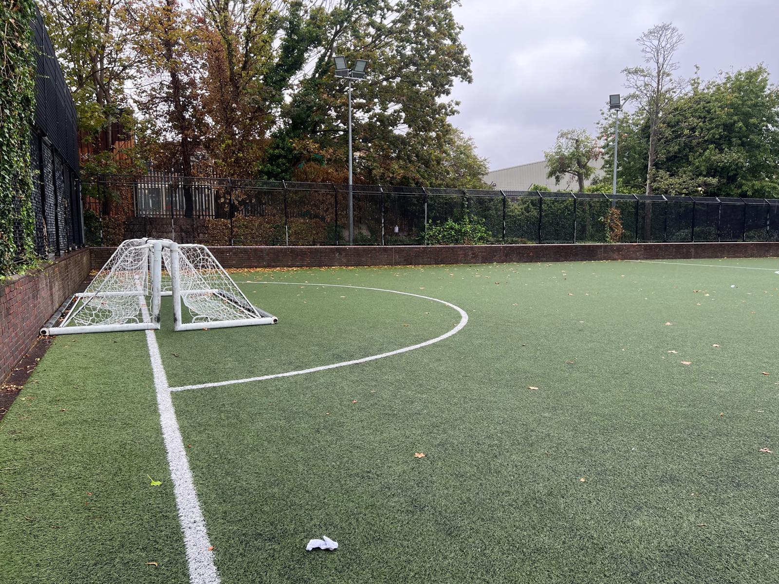 A corner of pitch 5 at Wandle Recreation Centre, with the low brick perimeter wall, two small goals stacked in the corner and the white touchline